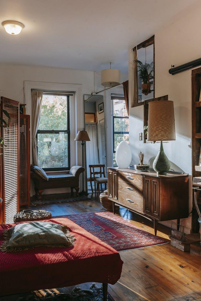 Interior of stylish vintage styled room with comfortable bed and classic wooden cabinet decorated with lamps and plants in sunlight